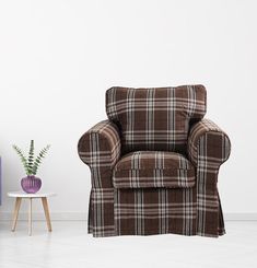 a brown chair sitting in front of a white wall next to a small table and purple vase