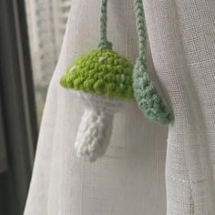 a crocheted mushroom hanging from the side of a white curtain with green trim