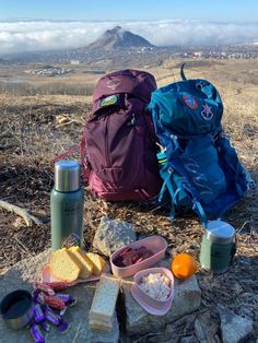 two backpacks sitting on top of a dry grass field next to food and drinks