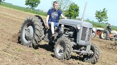 a man riding on the back of a gray tractor in a plow filled field