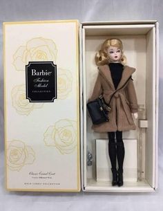 a barbie doll in a box with a black purse and coat on it's head