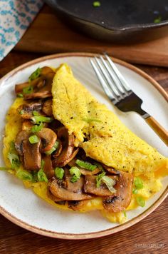 an omelet with mushrooms and green onions is on a plate next to a fork