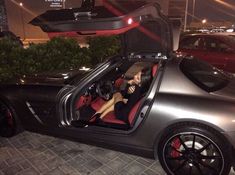 a woman sitting in the driver's seat of a silver sports car with its trunk open