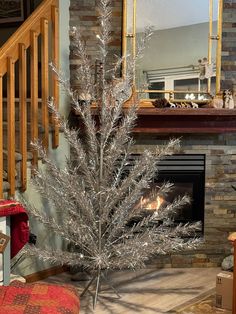 a silver christmas tree sitting in front of a fire place next to a stair case