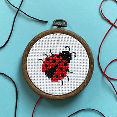 a cross stitch ladybug on a white circle with red thread