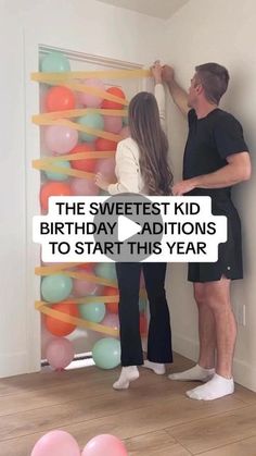 a man and woman standing next to each other in front of a birthday balloon wall