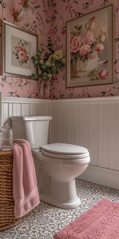 a white toilet sitting in a bathroom next to a pink rug and framed pictures on the wall