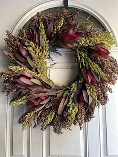 a wreath hanging on the front door of a house with dried flowers and foliage around it