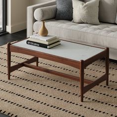 a living room with a couch, coffee table and books on the floor in front of a window