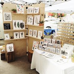 a table with pictures and cards on it at an outdoor art market under a tent