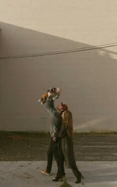 a man and woman walking down the street with a dog on their shoulders, one holding a teddy bear