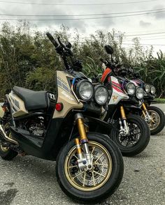 three motorcycles parked next to each other in a parking lot with trees and bushes behind them