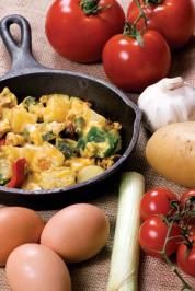 eggs, tomatoes, and other vegetables are on the table next to an iron skillet