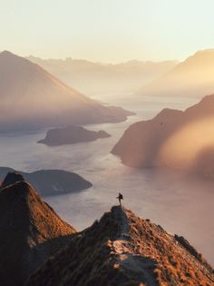 a person standing on top of a mountain next to a body of water with mountains in the background