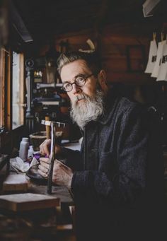 a man with a long beard and glasses is working on something in his workshop while looking at the camera