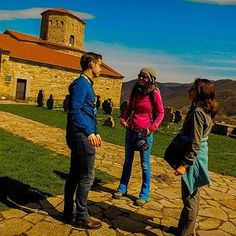 three people standing in front of a stone building with a clock tower on the top