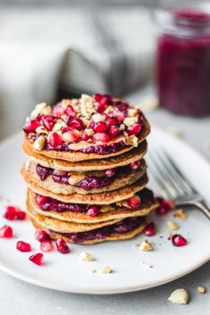 a stack of pancakes with pomegranates and nuts on a white plate