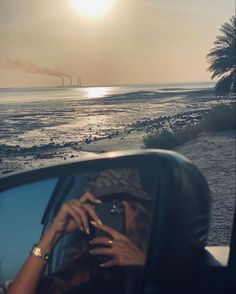 a woman taking a photo in the rear view mirror of a car on the beach