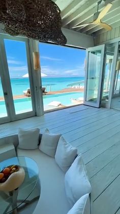 a living room filled with furniture next to an open window overlooking the ocean and beach