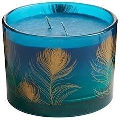 a blue glass candle with gold and green feathers on the inside, sitting in front of a white background