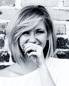 a black and white photo of a woman holding her hand to her mouth, smiling