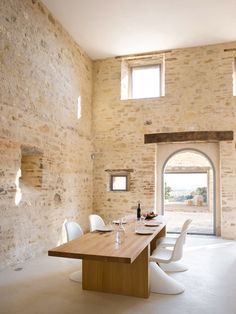 a dining room table and chairs in front of a stone wall with arched doorways