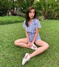 a woman sitting on the grass with her legs crossed and wearing white shoes, posing for a photo