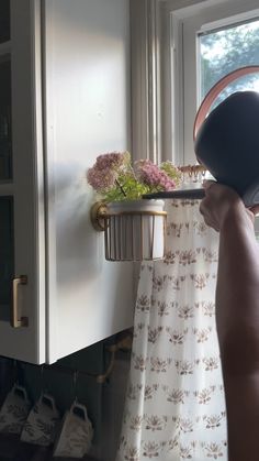 a person holding up a potted plant in front of a window