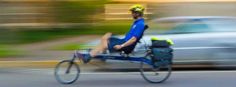 a man riding on the back of a blue bike down a street next to a silver car