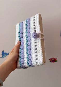 a hand is holding a crocheted book with a purple and white stripe on it