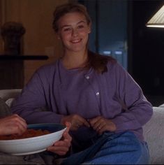 a man and woman sitting on a couch eating food from a bowl in front of them