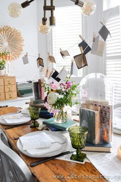 a wooden table topped with plates and vases filled with flowers next to a window