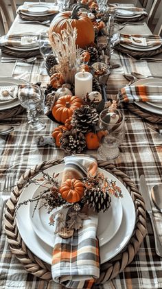 the table is set for thanksgiving dinner with pumpkins, pine cones and plaid napkins