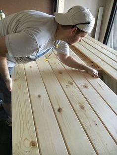 a man in white shirt and cap working on wooden table top with wood planks