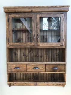 an old wooden cabinet with glass doors and drawers on the bottom shelf, against a white wall