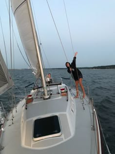 two people standing on the deck of a sailboat in the ocean with their arms up