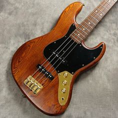 an electric bass guitar laying on top of a gray surface with gold hardware and strings