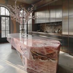 a large marble table in a kitchen with stainless steel appliances and cabinets, along with a vase filled with flowers