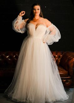 a woman in a white dress posing on a couch with her arms out and hands behind her head