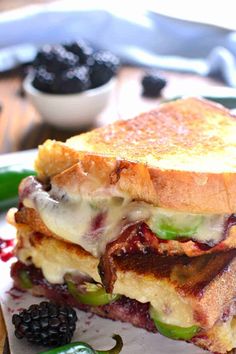 a grilled cheese sandwich with blackberries and green peppers on a plate next to some pickles