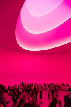 a large group of people standing in a room with pink lighting on the walls and ceiling