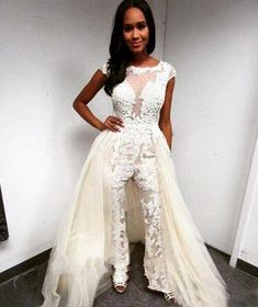 a woman standing in front of a white wall wearing a dress with flowers on it