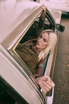 a woman leaning out the window of a car with her hand on the door handle