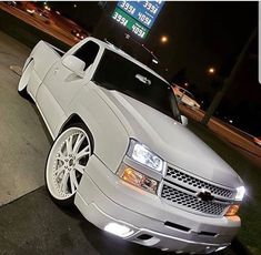 a white chevrolet camaro is parked in front of a gas station sign at night