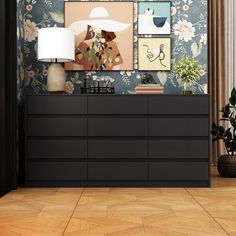 a black dresser sitting in front of a wall with pictures on it and a lamp next to it