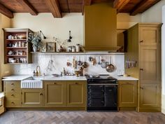 a kitchen with green cabinets and white counter tops, wooden flooring and exposed beams