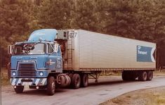 a blue semi truck driving down a road next to tall grass and trees in the background