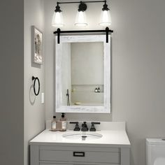 a bathroom with a sink, mirror and toilet in the corner is lit by two lights