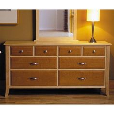 a wooden dresser sitting on top of a hard wood floor next to a lamp and mirror