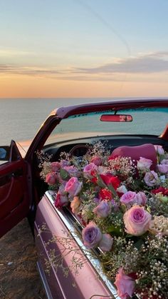 a car parked next to the ocean with flowers in the trunk and on the back